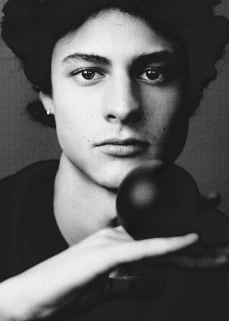 Close-up portrait of a young man holding a dark sphere in front of his face in monochrome