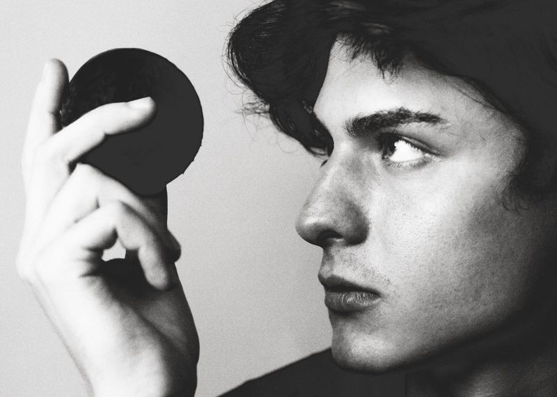 Close-up black and white portrait of a young man holding a dark spherical object near his face, photographed by Jesus Isnard for GQ Espana.