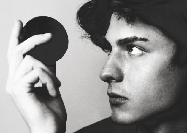 Close-up black and white portrait of a young man holding a dark spherical object near his face, photographed by Jesus Isnard for GQ Espana.
