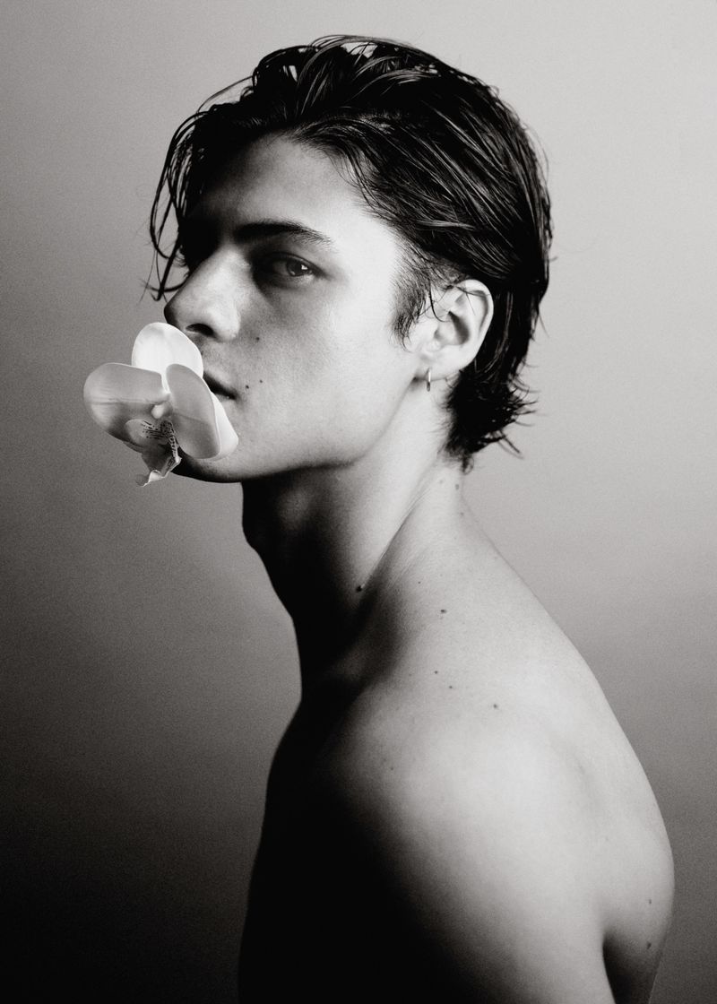 Profile portrait of a young man holding a white orchid between his lips for GQ Espana photographed by Jesus Isnard.