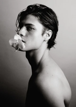 Profile portrait of a young man holding a white orchid between his lips for GQ Espana photographed by Jesus Isnard.