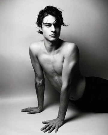 Black and white portrait of a shirtless young man resting on his hands against a seamless studio background