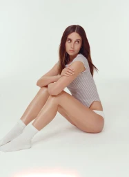 Woman in a striped short-sleeve top and white socks seated against a seamless white studio background