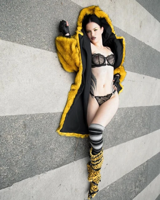 Woman poses in black lingerie and yellow fur coat on striped surface. Dark hair and lipstick. Fashion and portrait photography.