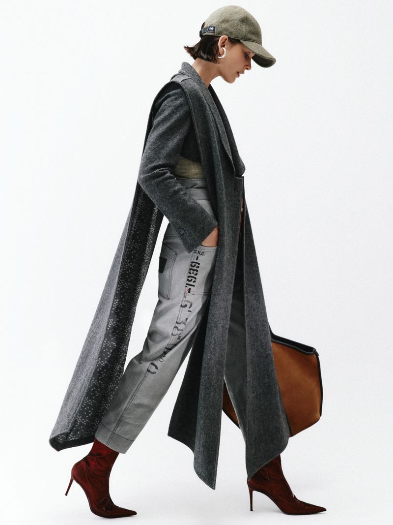 Model wearing a grey wool coat, printed trousers, baseball cap, and heeled boots against a white background