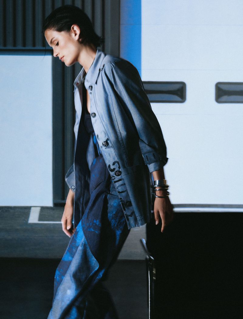 Model wearing a blue jacket and patterned pants standing against a modern architectural background