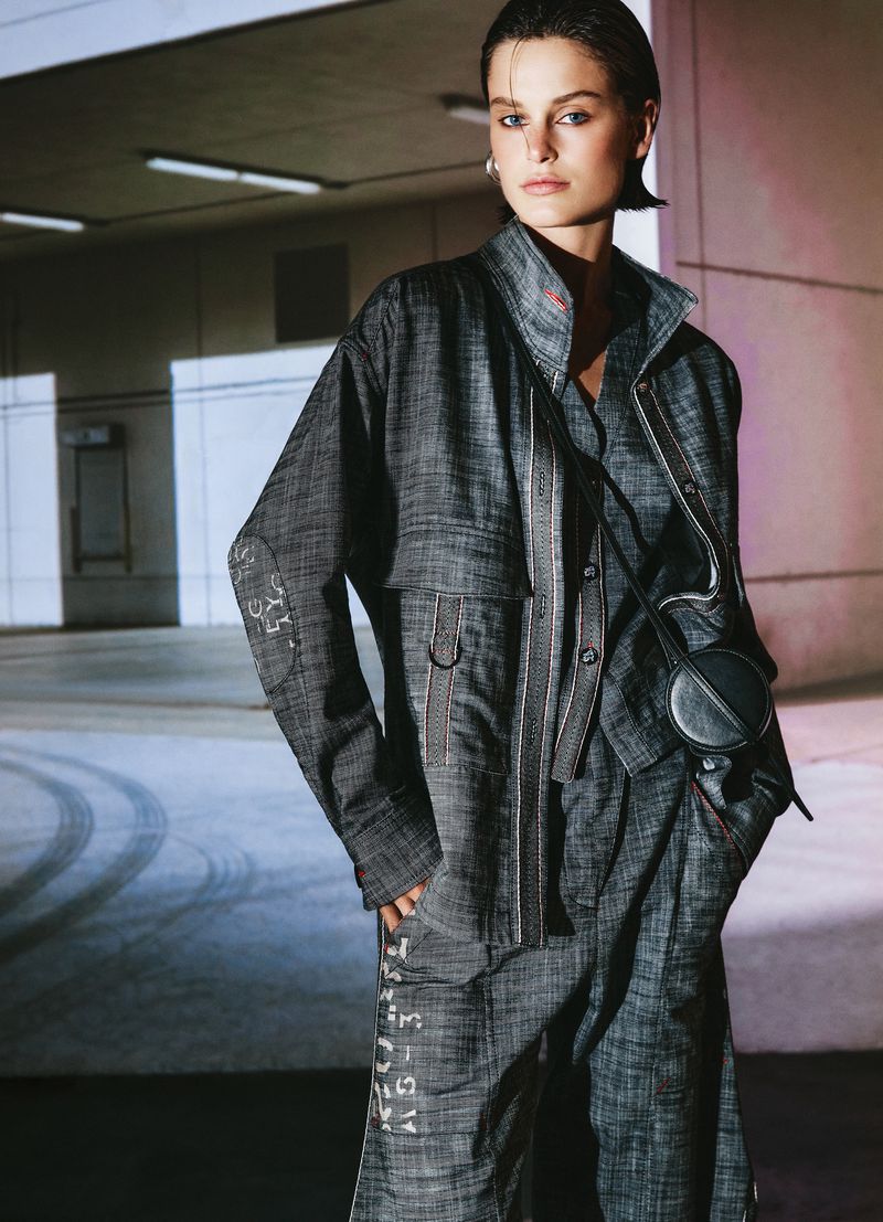 Model Lucianne Lijntje wearing grey textured utility jacket and trousers in a concrete parking structure for campaign.