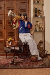 Young man in a blue and beige varsity jacket shouting into a yellow megaphone while seated indoors