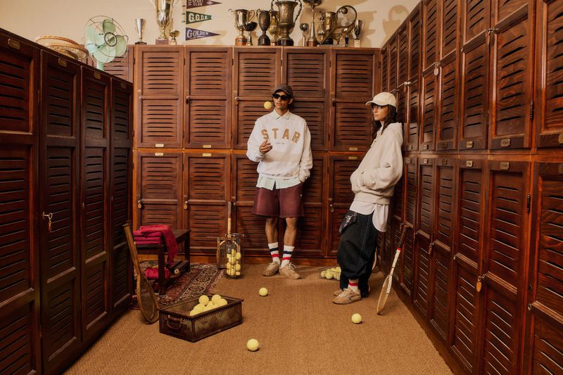 Two models in a wooden locker room surrounded by tennis equipment for the Golden Goose New Star campaign.