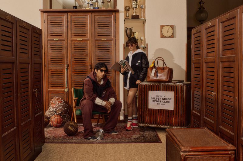 A man seated and a woman standing in a vintage wooden locker room with athletic equipment for the Golden Goose New Star Campaign.