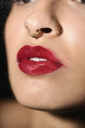 Close-up portrait of glossy red lips and septum piercing viewed through a wet glass pane with water droplets