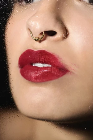 Close-up portrait of glossy red lips and septum piercing viewed through a wet glass pane with water droplets
