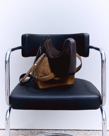 Two leather handbags resting on a black leather chair against a white seamless background