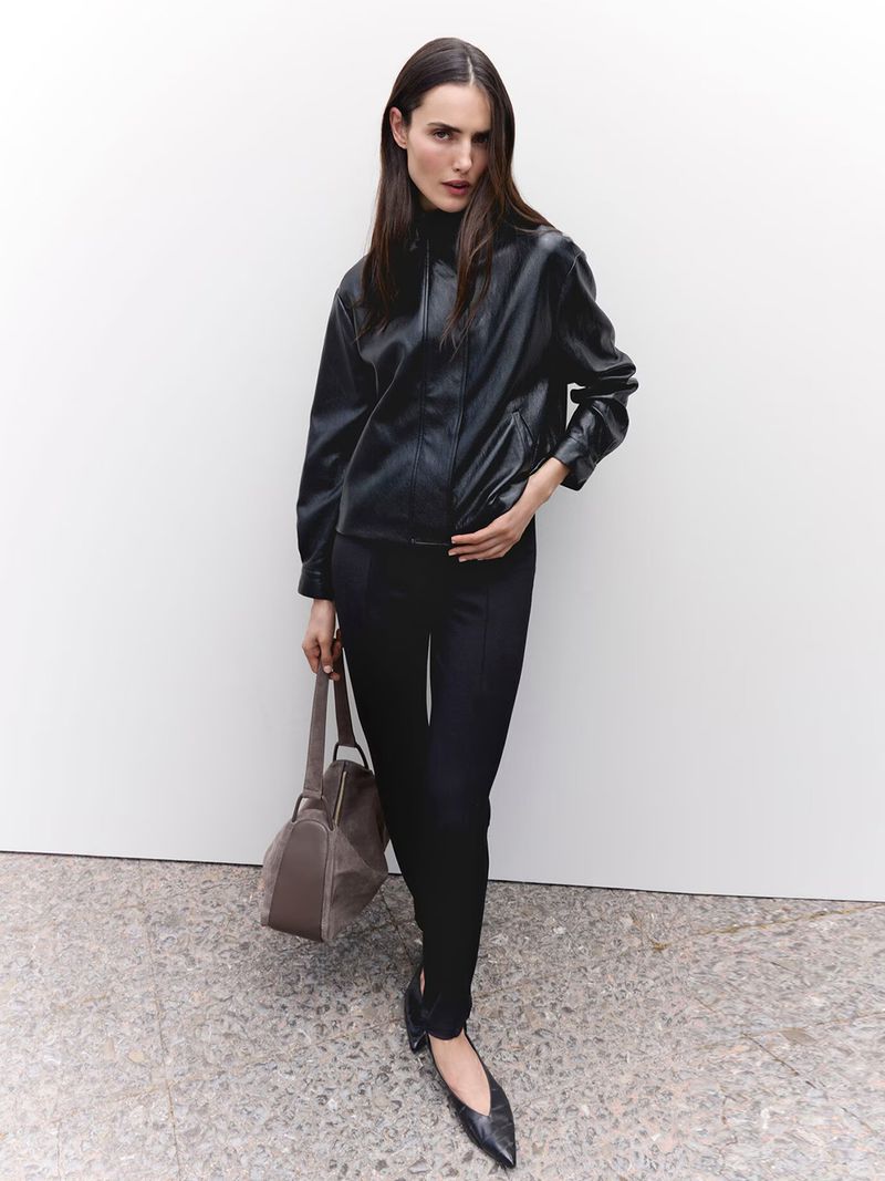 Model Blanca Padilla wearing a black leather jacket and trousers while holding a handbag against a plain background