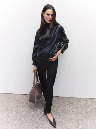 Model Blanca Padilla wearing a black leather jacket and trousers while holding a handbag against a plain background