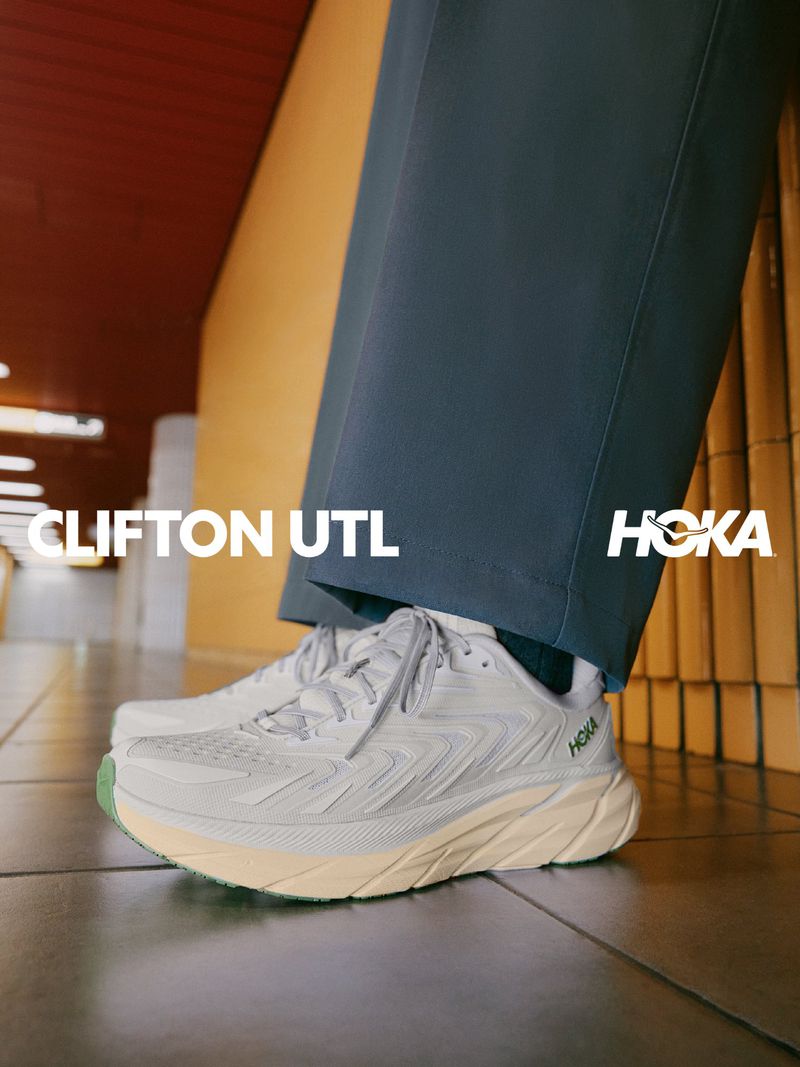Close-up shot of white running shoes worn with grey trousers, featuring overlaid typography reading CLIFTON UTL and HOKA.