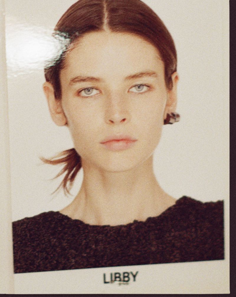 Portrait of Libby Taverner with brown hair tied back wearing a dark top against a white background.