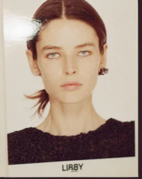 Portrait of Libby Taverner with brown hair tied back wearing a dark top against a white background.