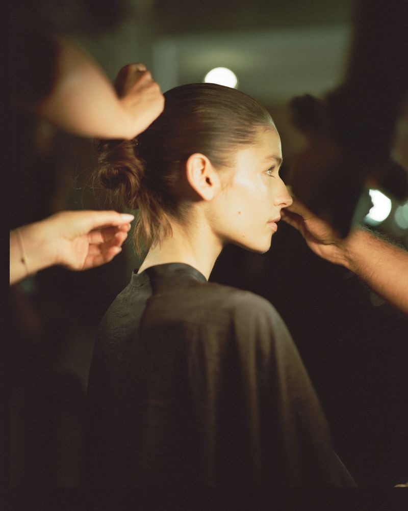 Backstage portrait of model Libby Taverner having her hair styled and makeup applied before a show at NYFW.