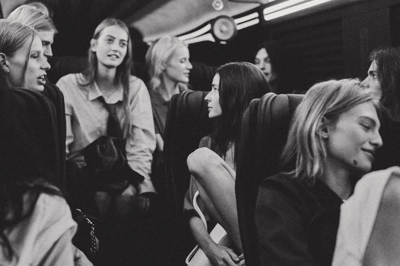 Black and white editorial photograph of multiple models seated inside a transit vehicle during NYFW.