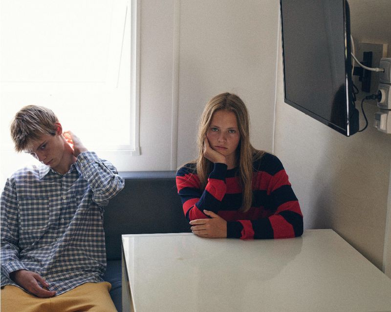 Young woman in a striped red and blue sweater seated at a table beside a man in a plaid shirt.