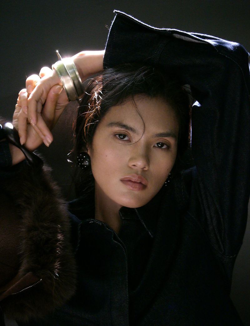 Model wearing dark denim jacket with hands raised, featuring silver bangle and fur texture detail