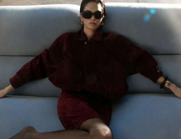 Model wearing a dark burgundy jacket and skirt seated on a pale blue sofa, photographed for Wonderland China.