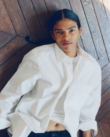 Model with long dark hair wearing a white button-down shirt lying on a wooden parquet floor