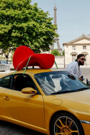 Larry June standing near a yellow sports car with a red designer chair strapped to the roof in Paris