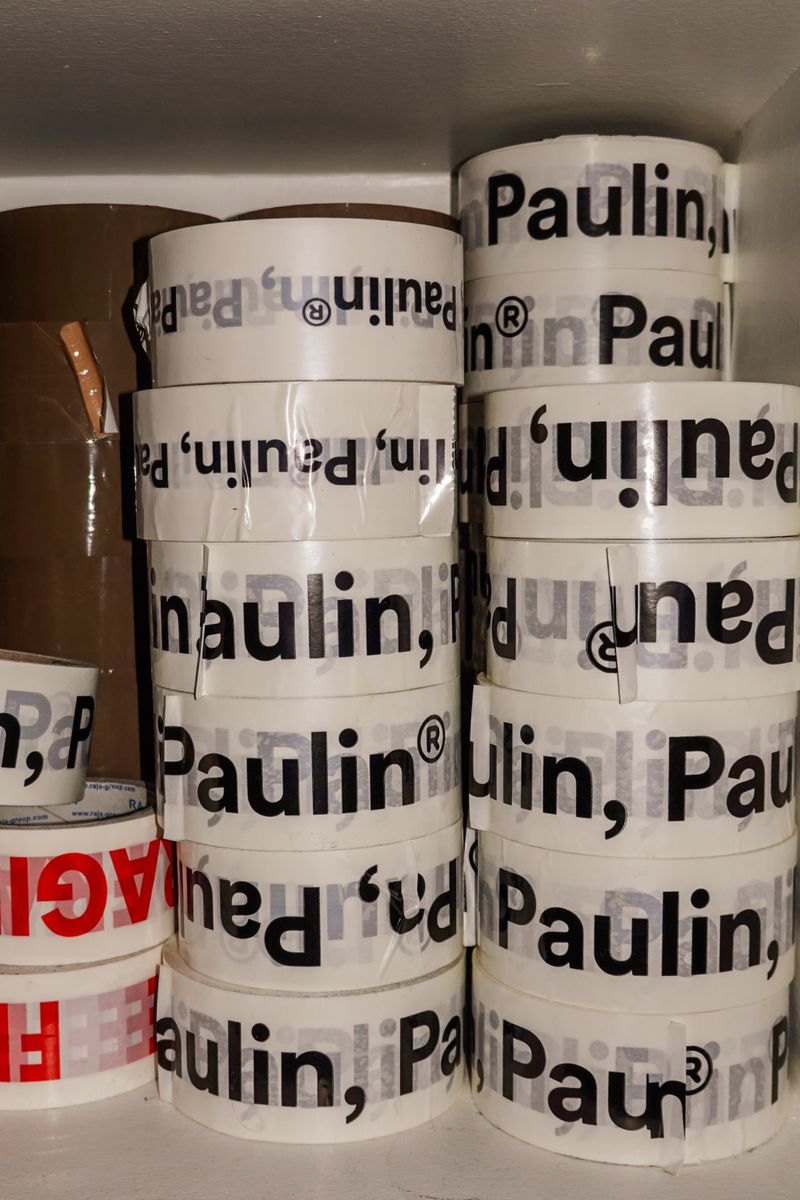 Stacks of white packing tape printed with the Paulin brand name stored tightly inside a storage shelf.