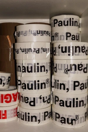 Stacks of white packing tape printed with the Paulin brand name stored tightly inside a storage shelf.