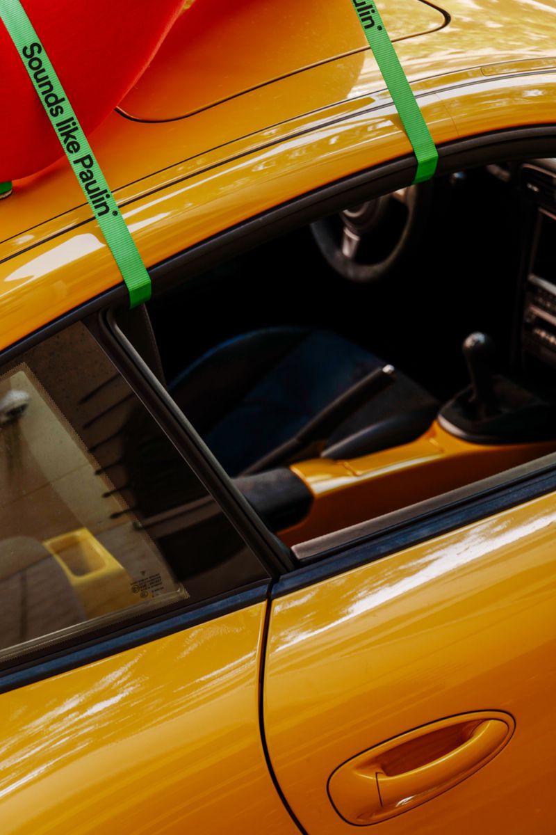 Close-up of a vibrant yellow sports car with green cargo straps securing an item on the roof.