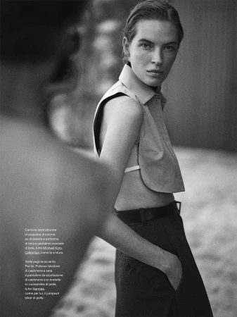 Model wearing a sleeveless collared top and trousers with a leather belt looking back over her shoulder in a black and white editorial photo.