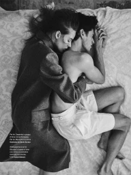 Monochrome fashion editorial image of a man and woman embracing while lying on a patterned bed