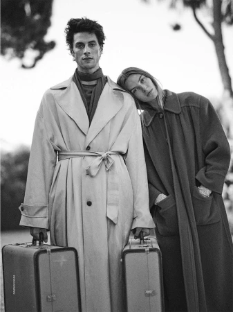 Black and white fashion editorial image featuring a male and female model holding vintage suitcases outdoors.