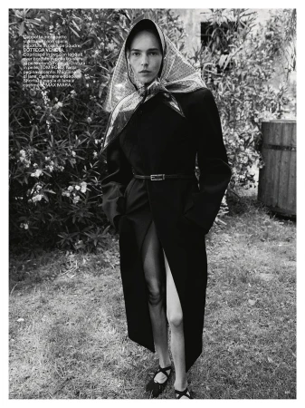 Model Puck Schrover wearing a dark coat and patterned headscarf outdoors in a garden for Marie Claire Italia