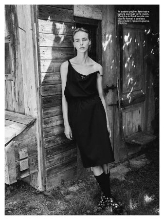 Model standing outdoors leaning against a weathered wooden rustic building wearing a black dress and socks