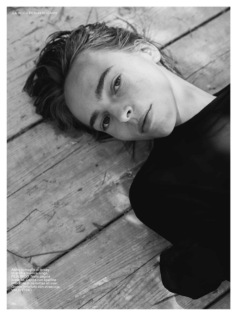 Close-up black and white portrait of a model lying on weathered wooden planks outdoors.