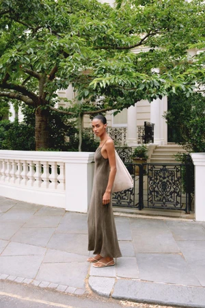 Model Sacha Quenby wearing a long olive slip dress and sandals on a paved street for Massimo Dutti