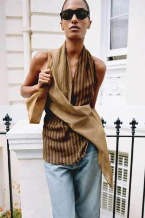 Model in sunglasses and striped top holding a shoulder bag in front of a white building exterior