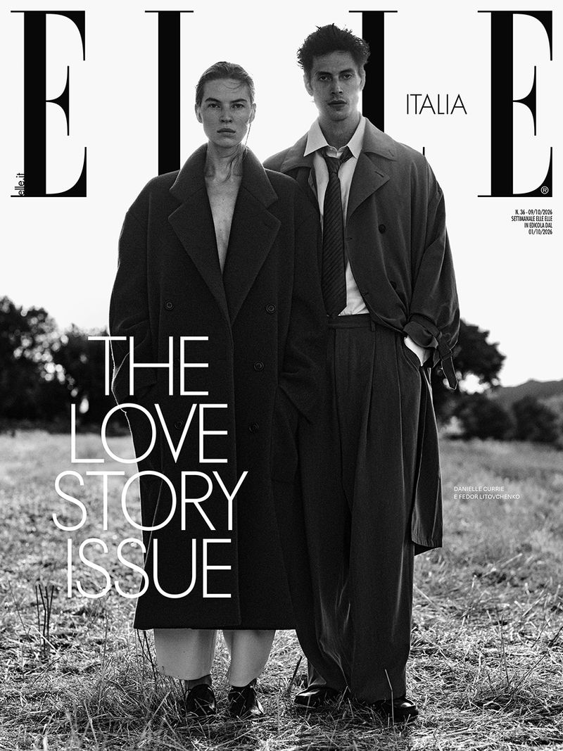 Black and white magazine cover featuring a woman and a man standing outdoors in a field wearing tailored coats.