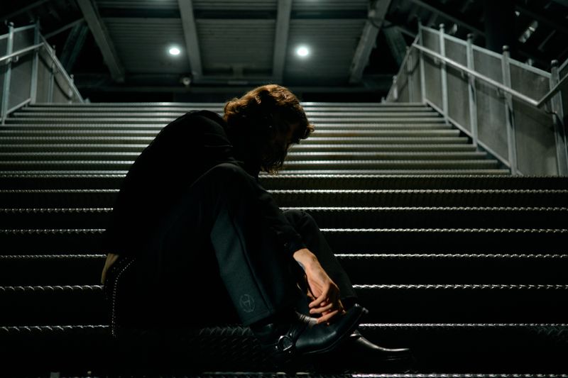 Model sitting on concrete steps at night wearing black clothing and boots for Wrangler X Slam Jam Blue Bell F/W 26