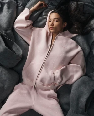 Model lying among grey hoodies wearing a light pink zip-up hoodie and matching sweatpants