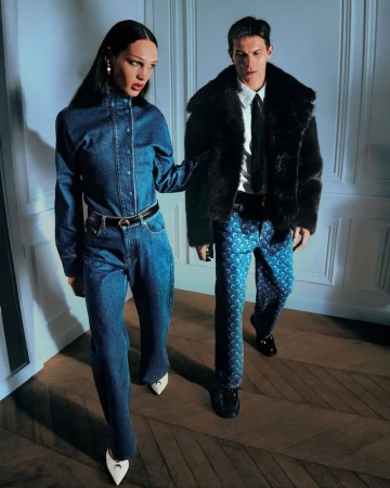 A stylish fashion editorial shot of a young adult couple in denim and faux fur coats, showcasing modern apparel in an indoor setting.