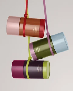 Three colorful cylindrical deodorant containers hanging suspended by colorful zip ties against a white background