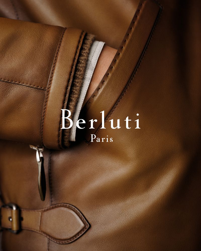 Tan leather Berluti jacket with visible stitching, buckle, and zipper pull. Close-up showcases the texture and craftsmanship of the luxurious material.