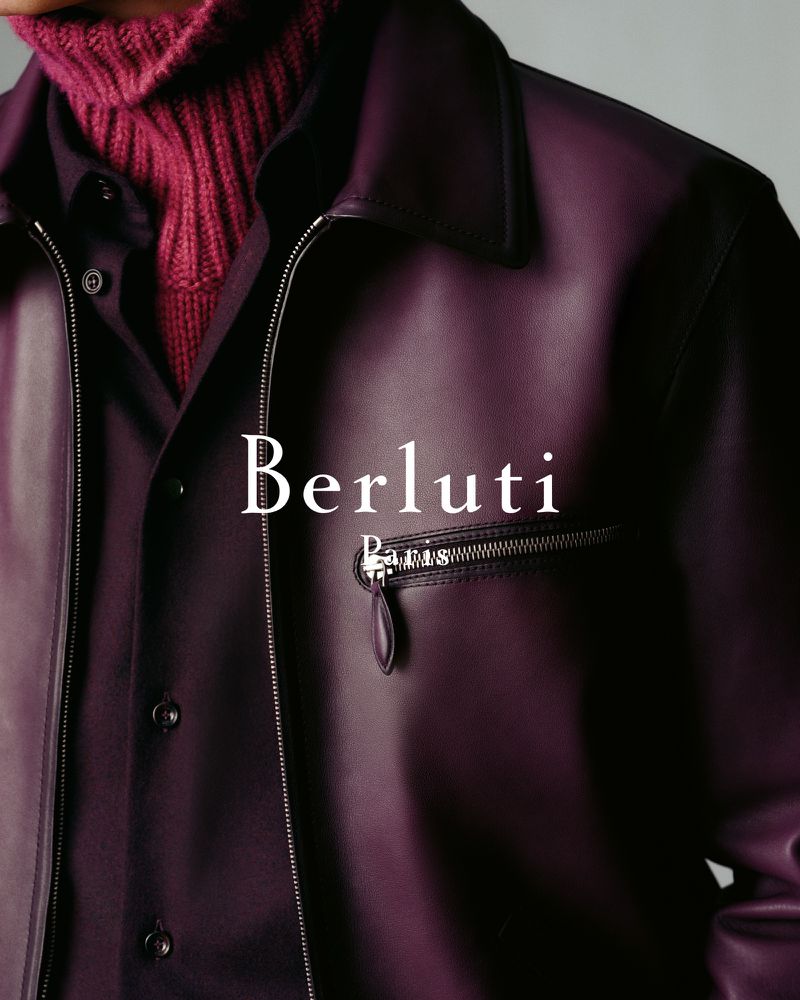Close-up studio shot of a person wearing a purple leather jacket and a maroon turtleneck, with the Berluti logo visible.