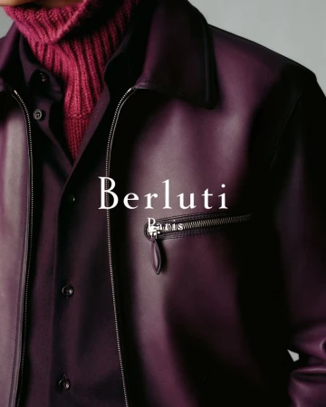 Close-up studio shot of a person wearing a purple leather jacket and a maroon turtleneck, with the Berluti logo visible.
