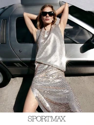 Model in sunglasses and metallic chainmail dress leaning against a silver car for Sportmax Fall-Winter 2026 campaign.