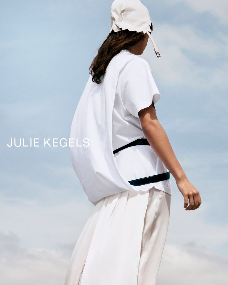 Model in white cap and white top standing against a pale sky for Julie Kegels FW26 fashion project